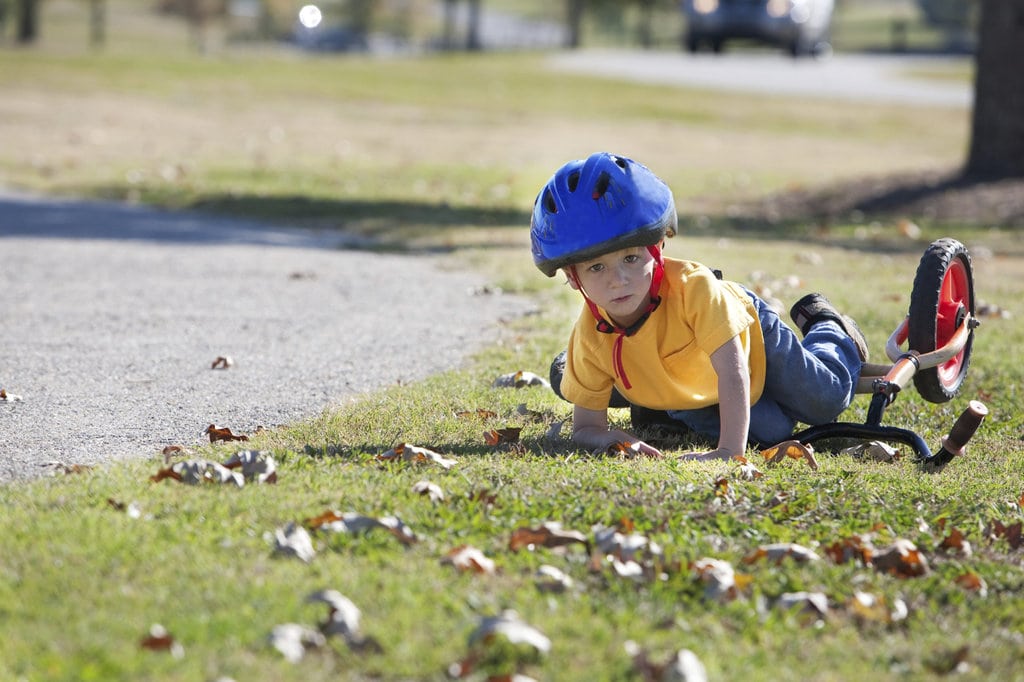 A young boy laying on the ground with his balance bike