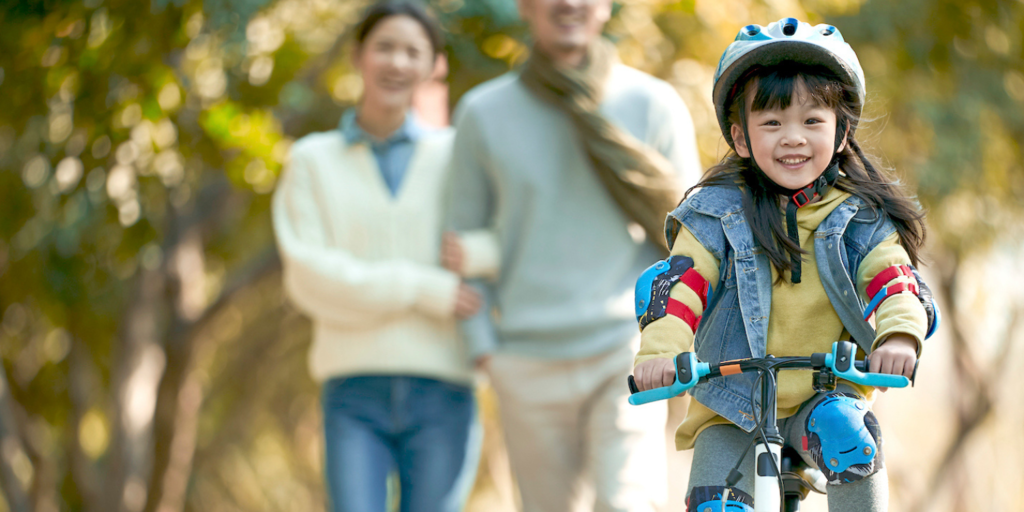 A young girls riding a balance bike with her parents in the background